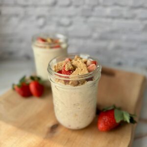 strawberry cheesecake overnight oats in a mason jar on wood cutting board.