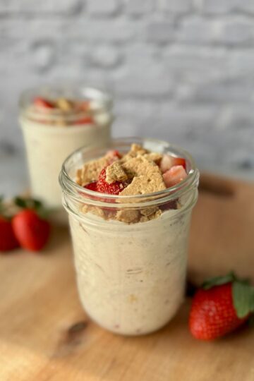 strawberry cheesecake overnight oats in a mason jar on wood cutting board.