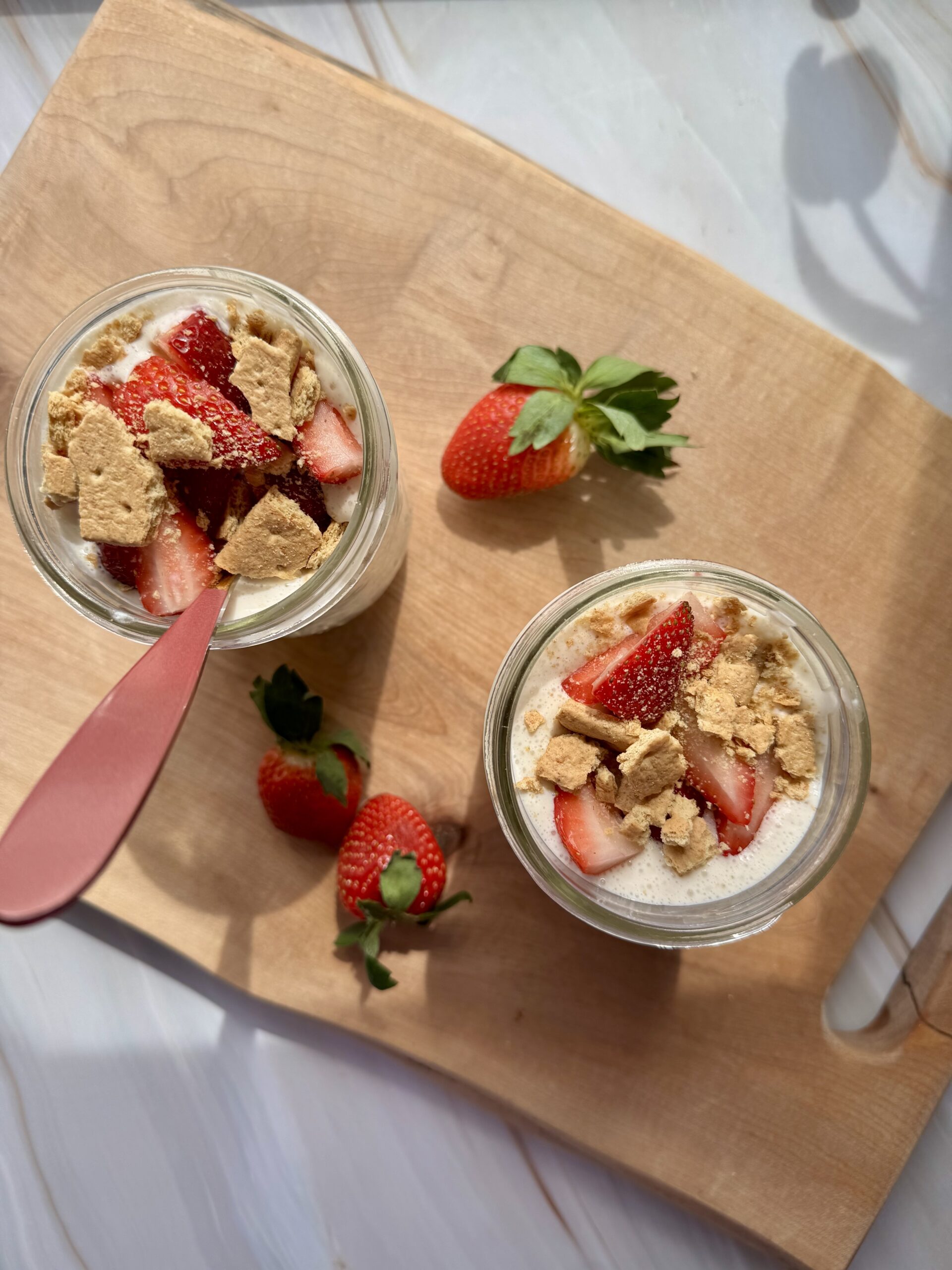 strawberry cheesecake oats in 2 mason jars on a wooden cutting board, looking top down.