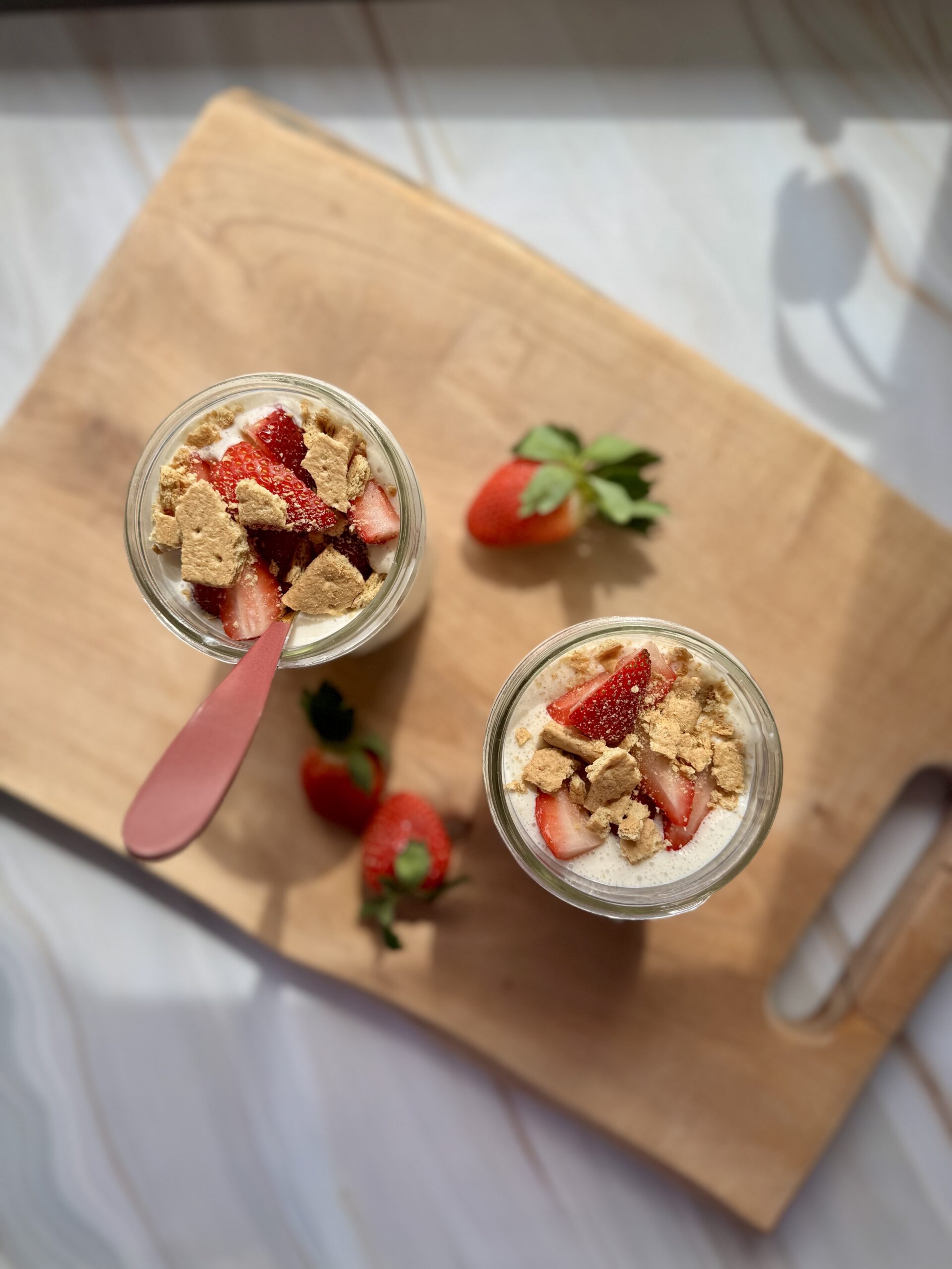 strawberry cheesecake oats in mason jars on wooden cutting board, looking top down.