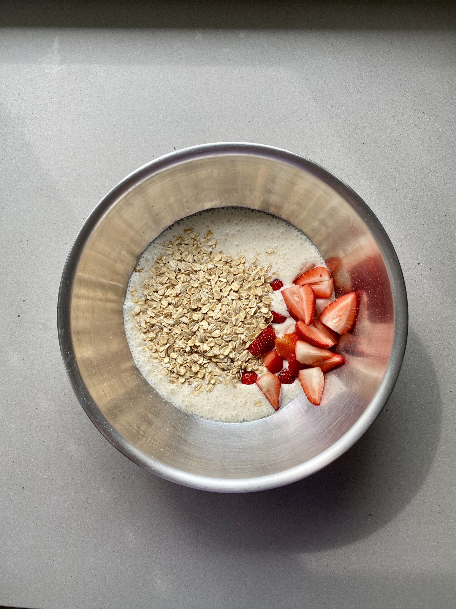 blended liquid ingredients in a large bowl with oats and strawberries, before mixing.
