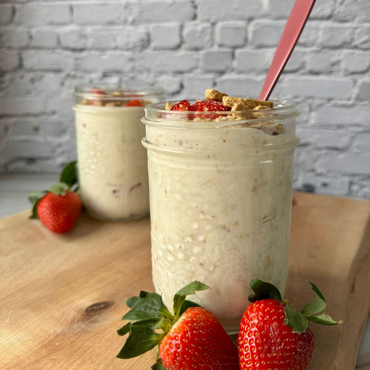 strawberry cheesecake oats in a mason jar on a wooden cutting board.