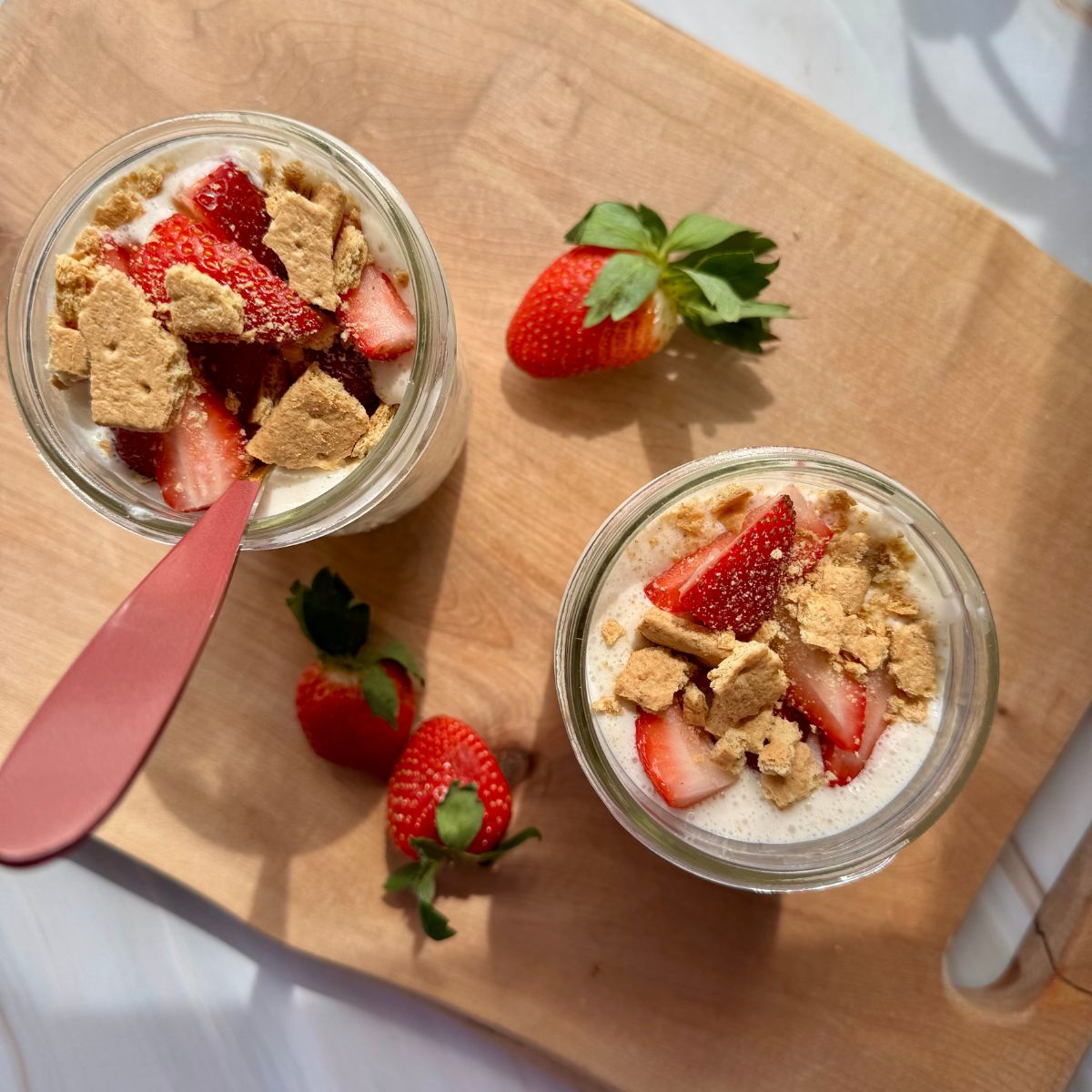 strawberry cheesecake oats in mason jars on a wooden cutting board.