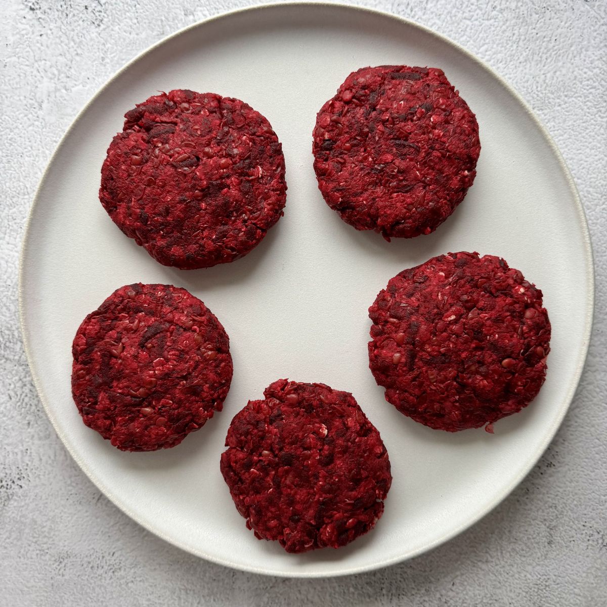 formed lentil and beetroot burgers on a white plate.