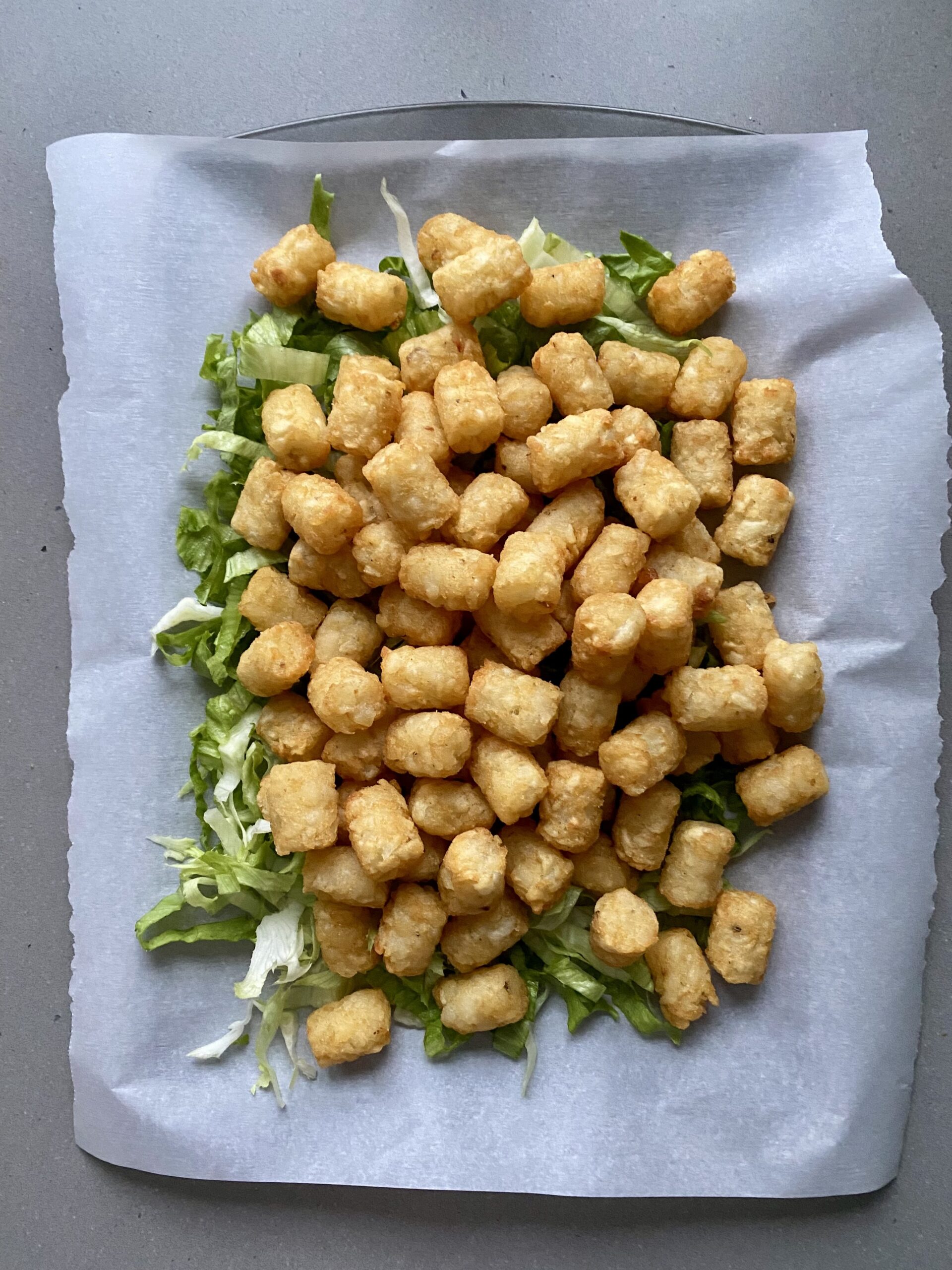lettuce and cooked tater tots layered on a baking sheet.