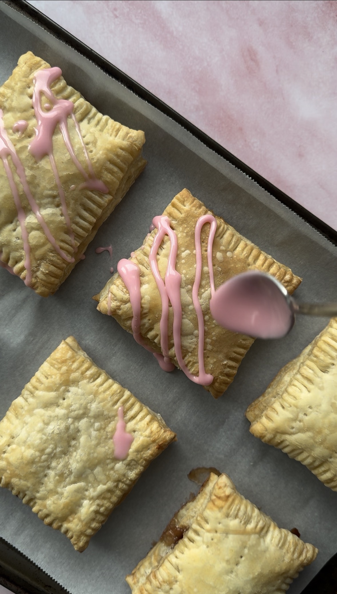 baked pop tarts with pink icing being drizzled on top.