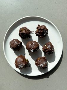 peanut butter date balls on a white plate covered in chocolate