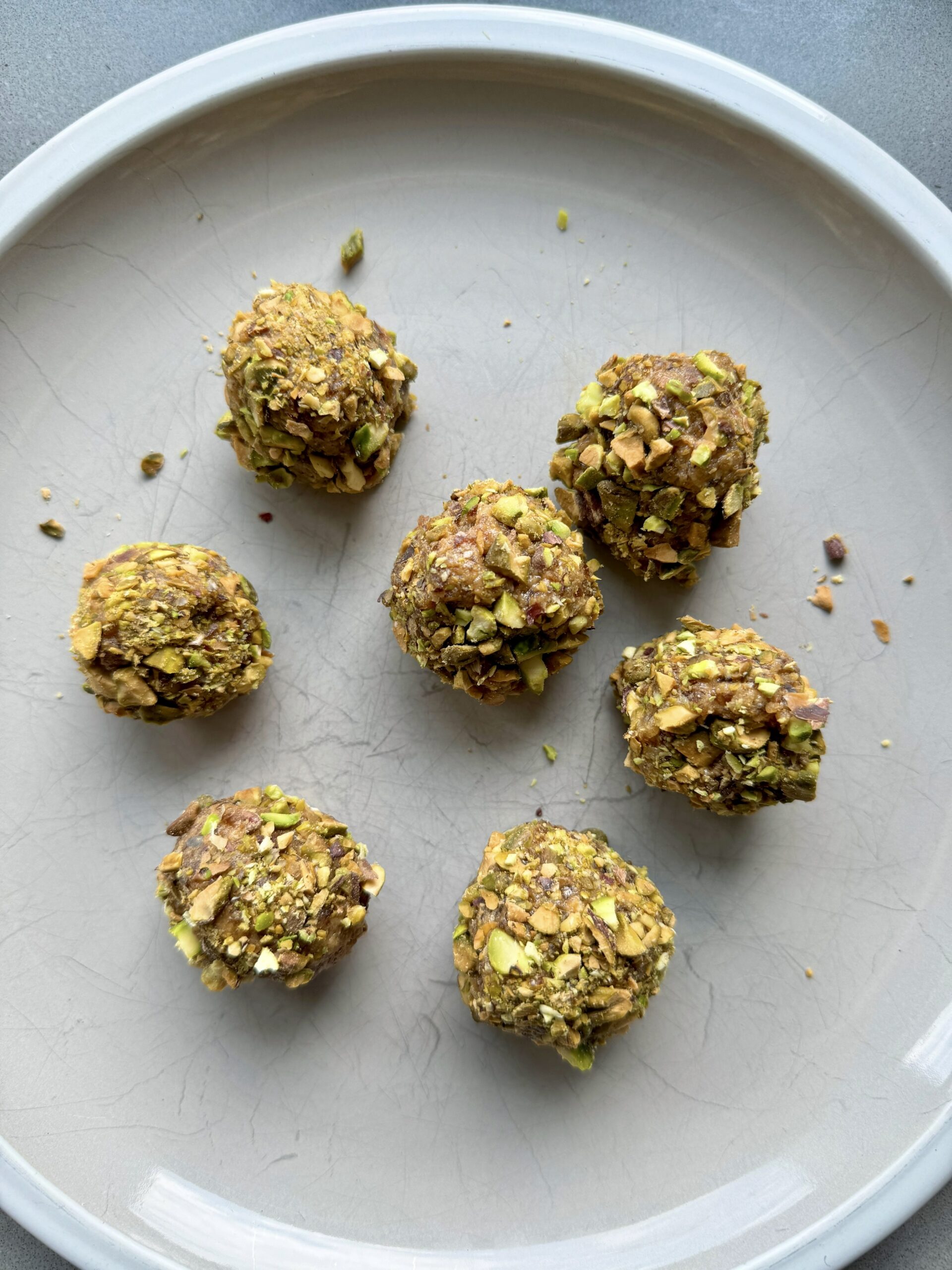seven date balls rolled in crushed pistachios on a plate.