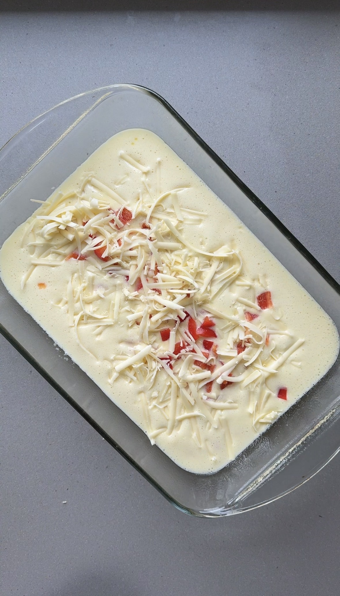 blended eggs and cottage cheese with shredded cheese and diced vegetables in a glass baking dish.