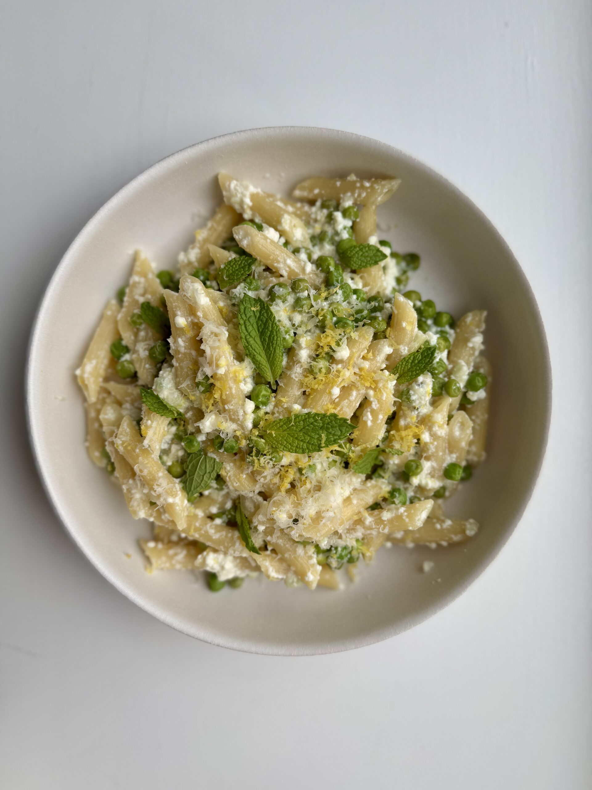 pea and ricotta pasta with garnishes in a white bowl.