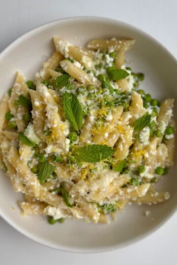 pea and ricotta pasta with garnishes in a white bowl.