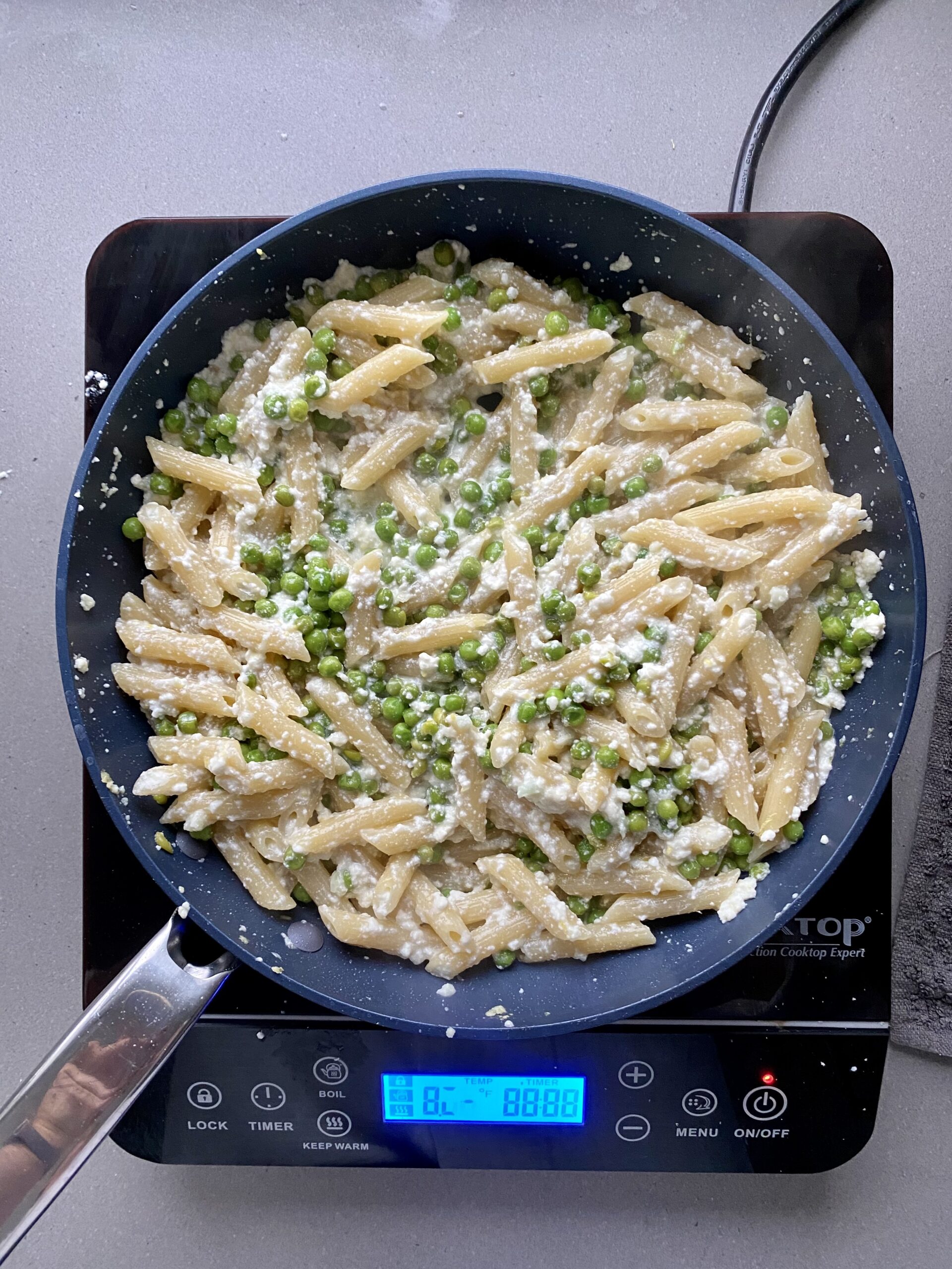 cooked penne pasta mixed with ricotta and peas in a frying pan.